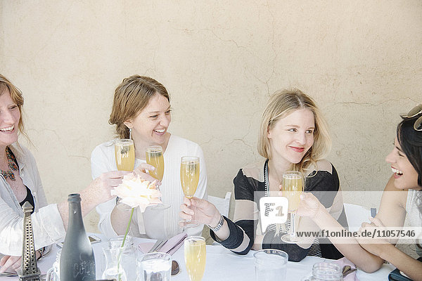 Four smiling women sitting at a table  holding glasses of champagne  toasting.