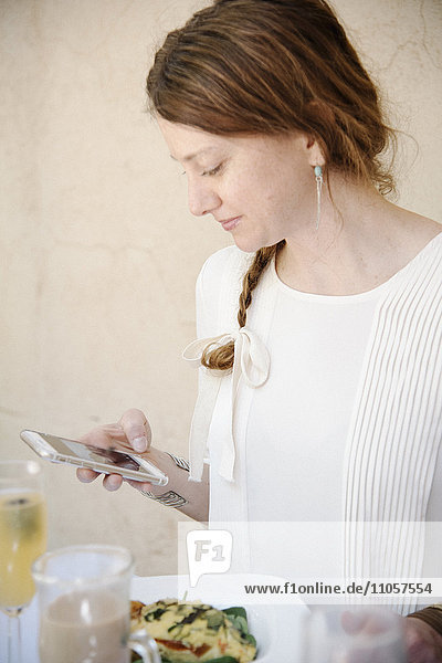 Porträt einer Frau mit langen  rotbraunen Haaren in einem Zopf  die auf ihr Handy schaut.