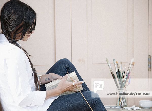 Junge Frau mit langen braunen Haaren  ein Skizzenbuch und einen Pinsel haltend.