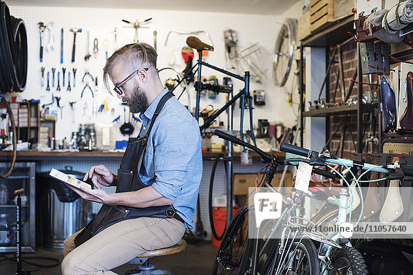 Ein Mann  der in einer Fahrradwerkstatt arbeitet und mit einem digitalen Tablett sitzt.