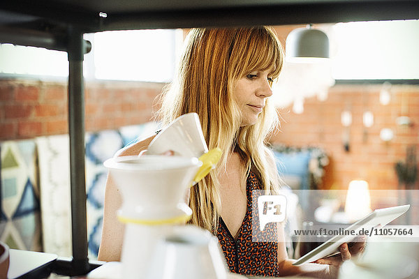 Frau in einem Geschäft  die ein digitales Tablett und einen kleinen Keramiktopf in der Hand hält.