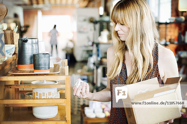 Frau in einem Geschäft  die einen kleinen Karton mit Waren in der Hand hält.