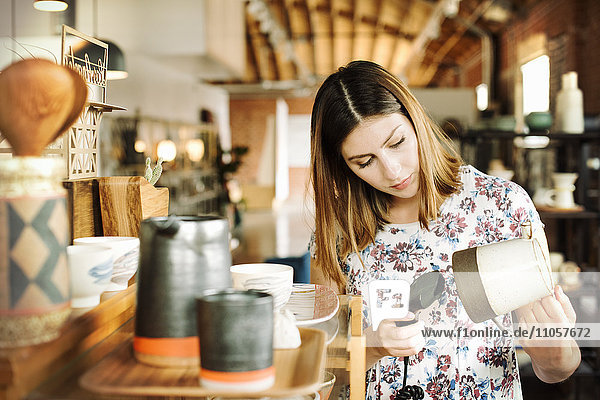 Junge Frau in einem Geschäft  die den Strichcode einer Keramikkanne mit einem Strichcode-Scanner einscannt.