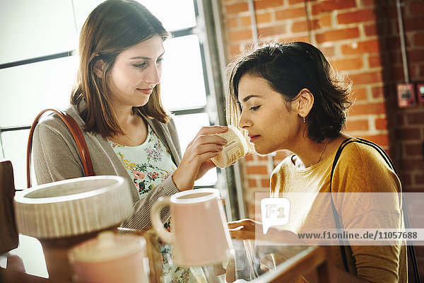Zwei junge Frauen in einem Geschäft  die an einem Glas Lavendelsalbe riechen.