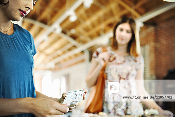 Zwei junge Frauen in einem Geschäft  die ein Kreditkartenlesegerät benutzen.
