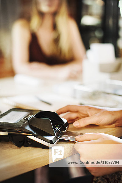 Nahaufnahme einer Frau  die in einem Geschäft ein Kreditkartenlesegerät benutzt.