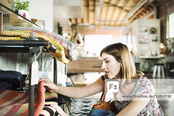 Junge Frau in einem Geschäft  die Teppiche in einem Regal betrachtet.