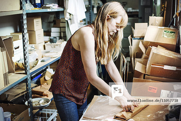 Woman with long blond hair standing in the store room of a shop  wrapping merchandise in brown paper.