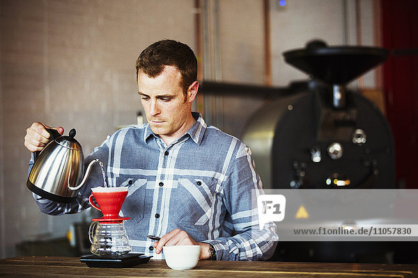 Spezialisiertes Kaffeehaus. Ein Mann,  der mit Hilfe eines Filterpapiers Kaffee brüht und ihn trinkt.