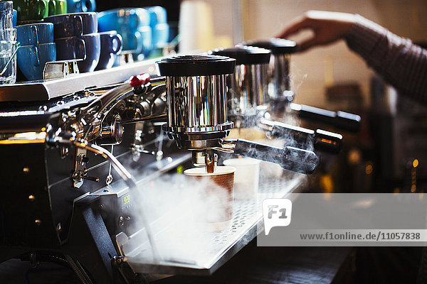 Spezialisiertes Kaffeehaus. Eine Person  die an einer großen Kaffeemaschine arbeitet  mit drei Perkolationsbehältern  Griffen und einem Rohr  das Dampf abgibt.