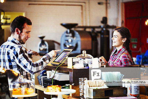 Spezialisiertes Kaffeehaus. Ein Mann hinter der Theke  der einen Touchscreen benutzt  um Transaktionen aufzuzeichnen  und eine Kundin.