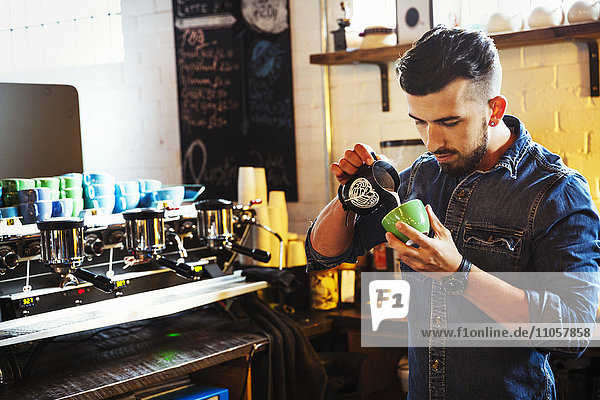Specialist coffee shop. A man preparing cappuccino creating froth patterns in a coffee cup.