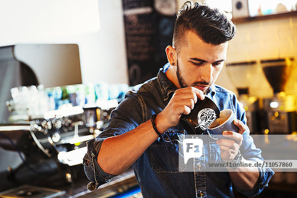 Spezialisiertes Kaffeehaus. Ein Mann  der Cappuccino zubereitet und Schaummuster in einer Kaffeetasse erzeugt.