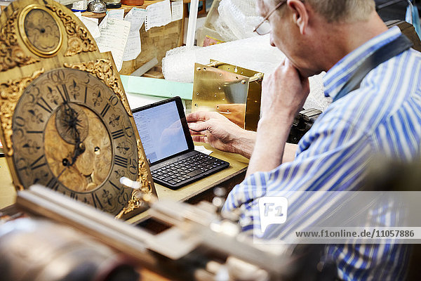 Ein Uhrmacher in seiner Werkstatt mit einem Laptop.