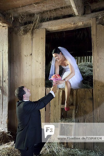Brautpaar  Braut schaut aus Heustadel  Bräutigam überreicht Blumenstrauß