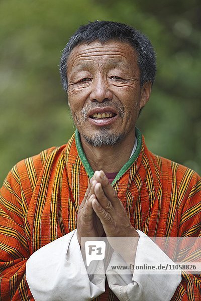 Mann  58 Jahre  in Gho-Tracht mit gefalteten Händen  Porträt  Jakar  Bumthang Valley  Königreich Bhutan