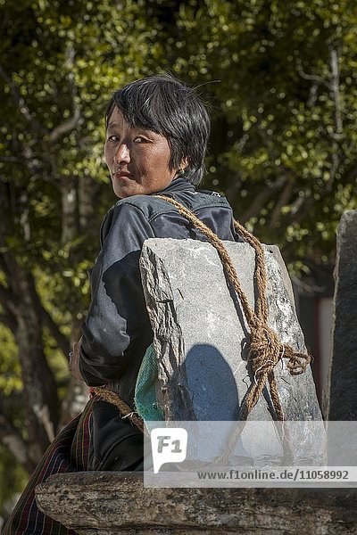 Eine Frau ruht sich aus  mit Baumaterial  Steinplatte auf dem Rücken  Himalaya-Region  Königreich Bhutan