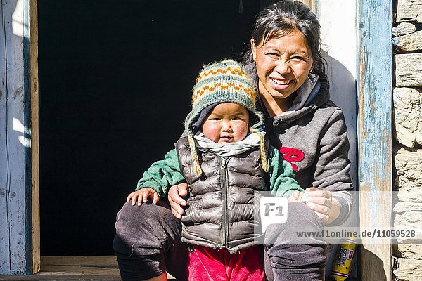 Portrait einer lächelnden jungen nepalesischen Mutter mit ihrem Kind  die in einem Hauseingang sitzen  Chheplung  Solo Khumbu  Nepal  Asien