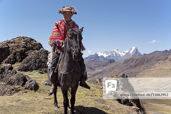 Indio mountain guide with colorful poncho riding on horse in the mountains Andes Lares near Cusco Peru South America