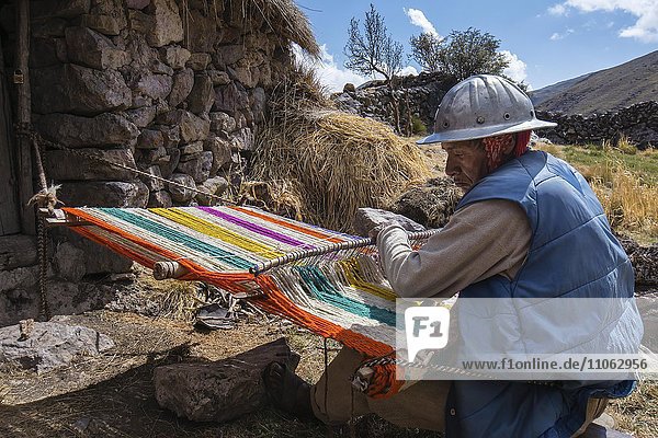Old Indio man with helmet weaving a colorful rug with a simple loom  in Cusco  Peru  South America