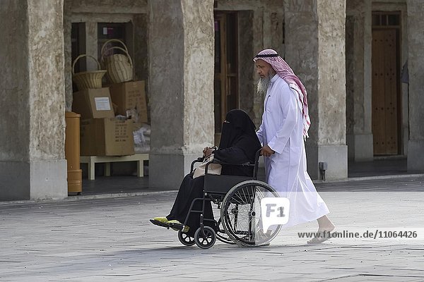 Einheimischer Mann schiebt eine verschleierte Frau im Rollstuhl  Doha  Katar  Asien