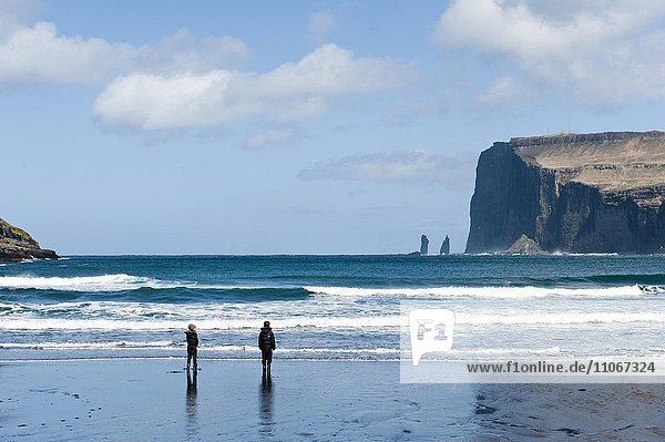 Two people on the black sand beach of Tjørnuvík  Streymoy  behind Risin and Kellingin spiers in the sea  Eysturoy cliffs  Faroe Islands  Føroyar  Denmark  Europe