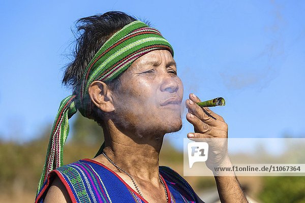 Mann in traditionellem Kostüm raucht Zigarre  Volksstamm der Phnong  Ethnische Minderheit  Pnong  Bunong  Senmonorom  Sen Monorom  Provinz Mondulkiri  Kambodscha  Asien