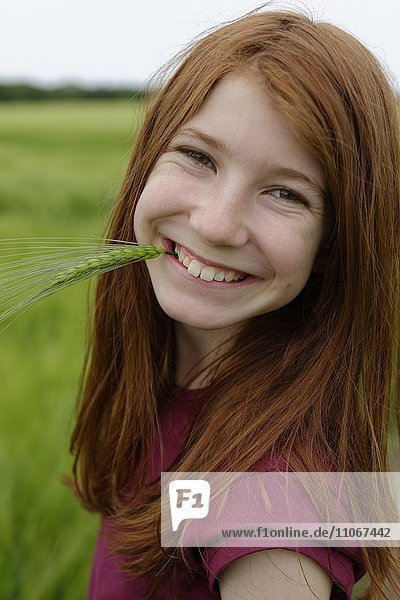 Smiling teenage girl  laughing  with barley grass in her mouth  Germany  Europe