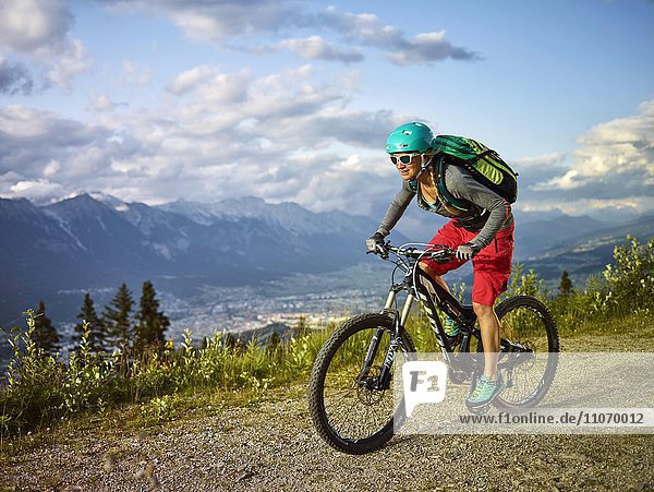 Mountain biker with a helmet riding on a gravel road  Mutterer Alm near Innsbruck  Northern chain of the Alps behind  Tyrol  Austria  Europe