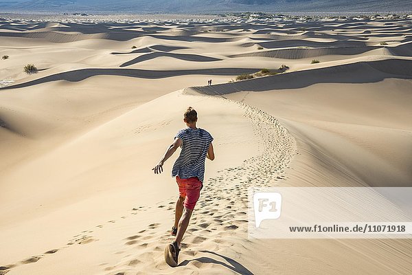 Junger Mann  Tourist läuft eine Sanddüne hinunter  Mesquite Flat Sand Dunes  Sanddünen  Death Valley  Death-Valley-Nationalpark  Kalifornien  USA  Nordamerika