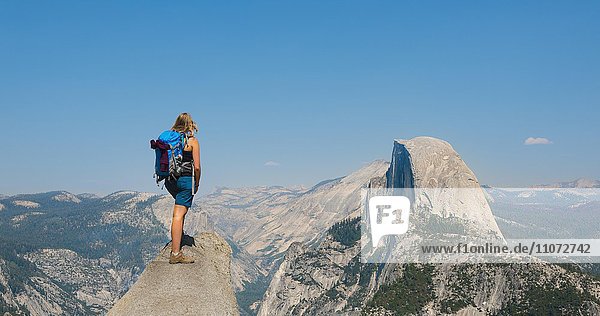 Wanderin steht auf einem Felsvorsprung und blickt auf Half Dome  Ausblick vom Glacier Point  Yosemite National Park  Kalifornien  USA  Nordamerika