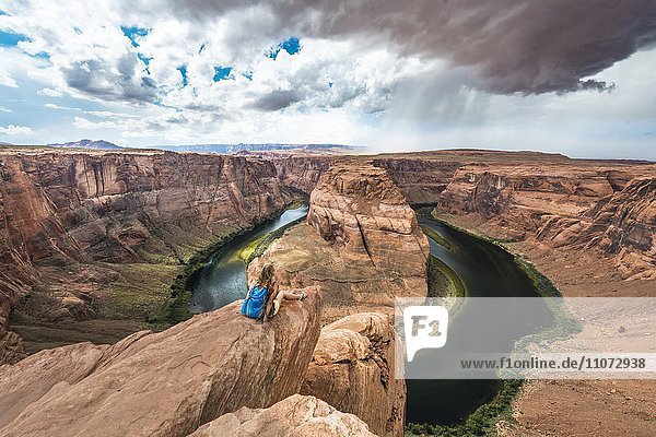 Touristin sitzt auf einem Felsen und schaut über das Horseshoe Bend  Flussschleife des Colorado River  King Bend  Glen Canyon National Recreation Area  Page  Arizona  USA  Nordamerika