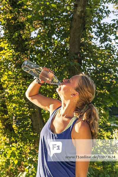 Junge Frau in Sportkleidung trinkt Wasser aus einer Flasche Bayern Deutschland Europa