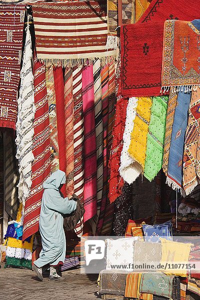 Woman in front of a shop with colourful carpets in the souks of Marrakesh  Morocco  Africa