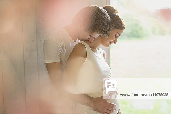 Affectionate pregnant couple hugging at window