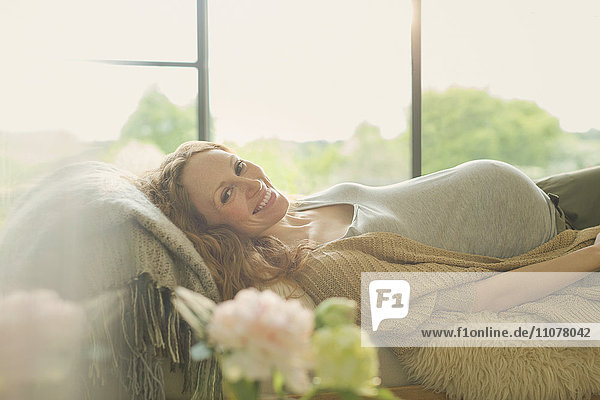 Portrait lächelnde schwangere Frau auf dem Sofa liegend