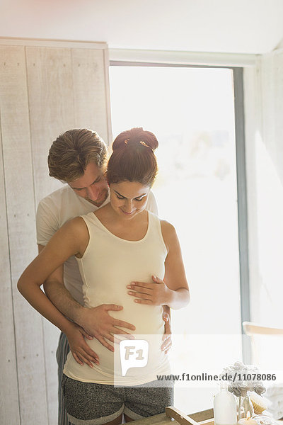 Pregnant couple holding stomach in sunny bathroom