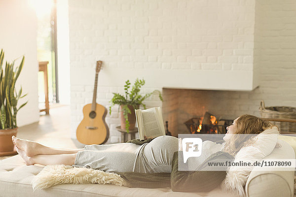 Serene pregnant woman laying on chaise next to fireplace in living room