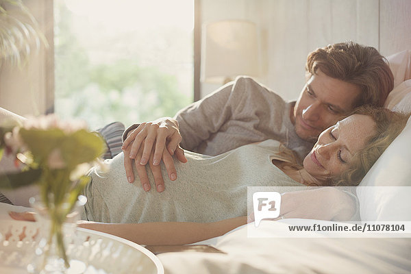 Serene pregnant couple holding stomach on bed