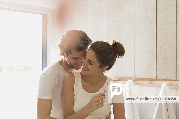 Affectionate couple brushing teeth in sunny bathroom