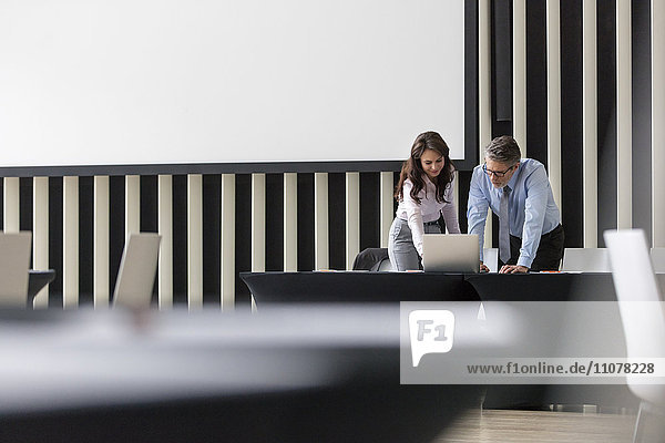 Businessman and businesswoman using laptop in conference room
