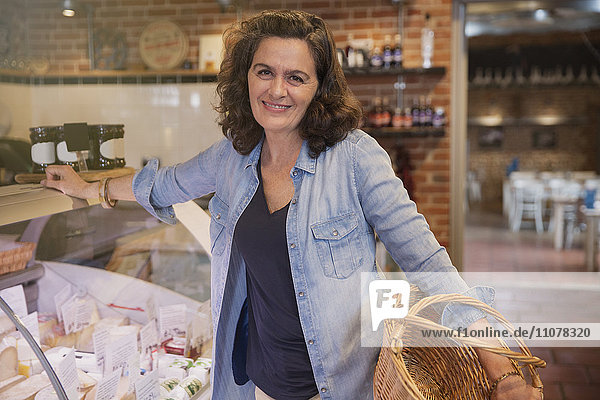 Portrait lächelnde Frau mit Korb auf Käsevitrine auf dem Markt