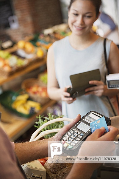 Frau beobachtet die Verkäuferin eines Lebensmittelgeschäfts mit einem Kreditkartenautomaten.