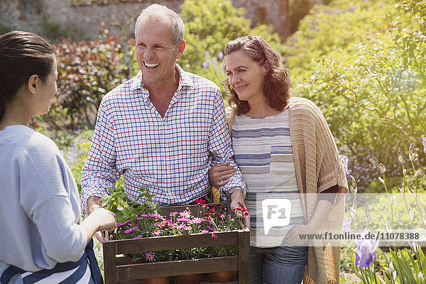 Pflanzenpflegerin hilft lächelndem Paar mit Blumen im Garten