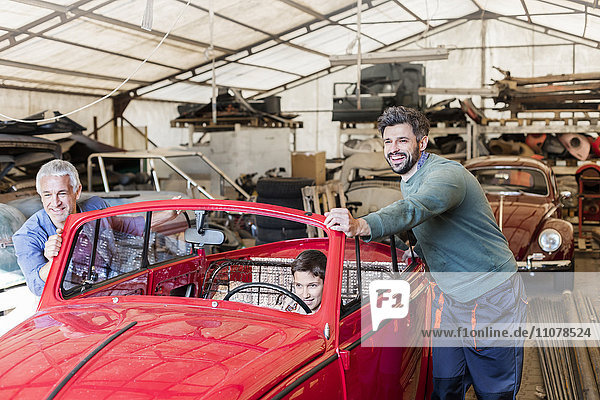 Lächelnde Mechaniker schieben Jungen im Oldtimer in Autowerkstatt