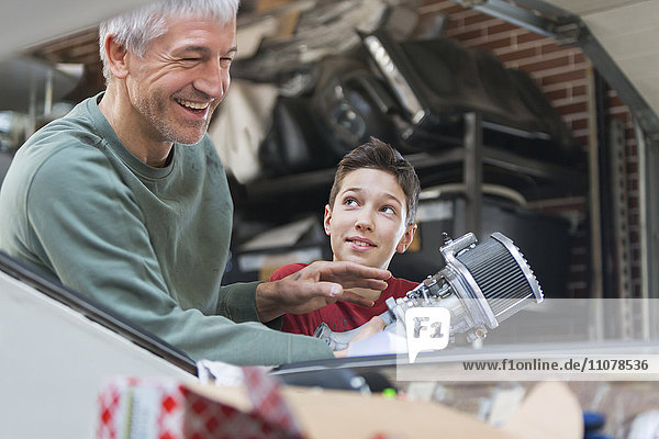 Lächelnder Vater und Sohn beim Reparieren des Motors in der Autowerkstatt