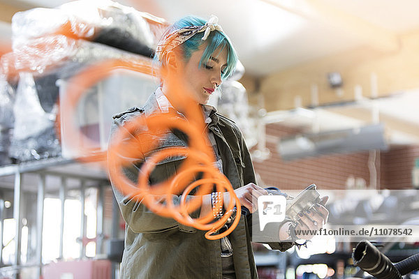Junge Mechanikerin mit blauen Haaren mit Geräten in der Autowerkstatt