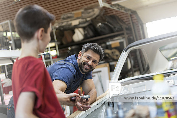 Lächelnder Vater nimmt Werkzeug vom Sohn in der Autowerkstatt