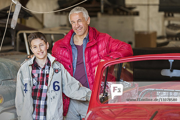 Portrait lächelnder Vater und Sohn neben dem Oldtimer in der Autowerkstatt