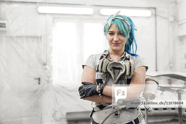 Portrait confident young woman with blue hair with paint gun in auto body shop